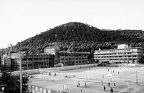 写真5-4-15 グラウンドから衣笠山と建設中の存心館を望む(1980年頃)