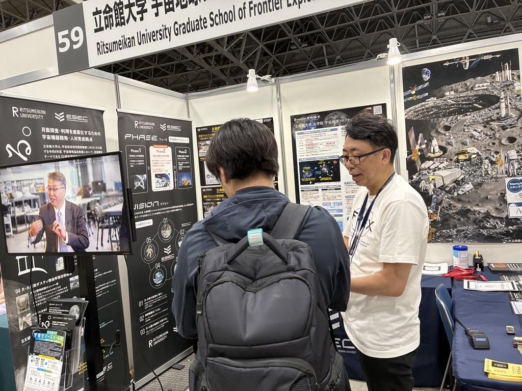 ブースに訪れる来場者と対話する佐伯センター長(右)　